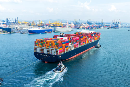 Container ship assisted by tugboats near a busy container port
